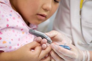 Young child receiving help testing blood sugar level.